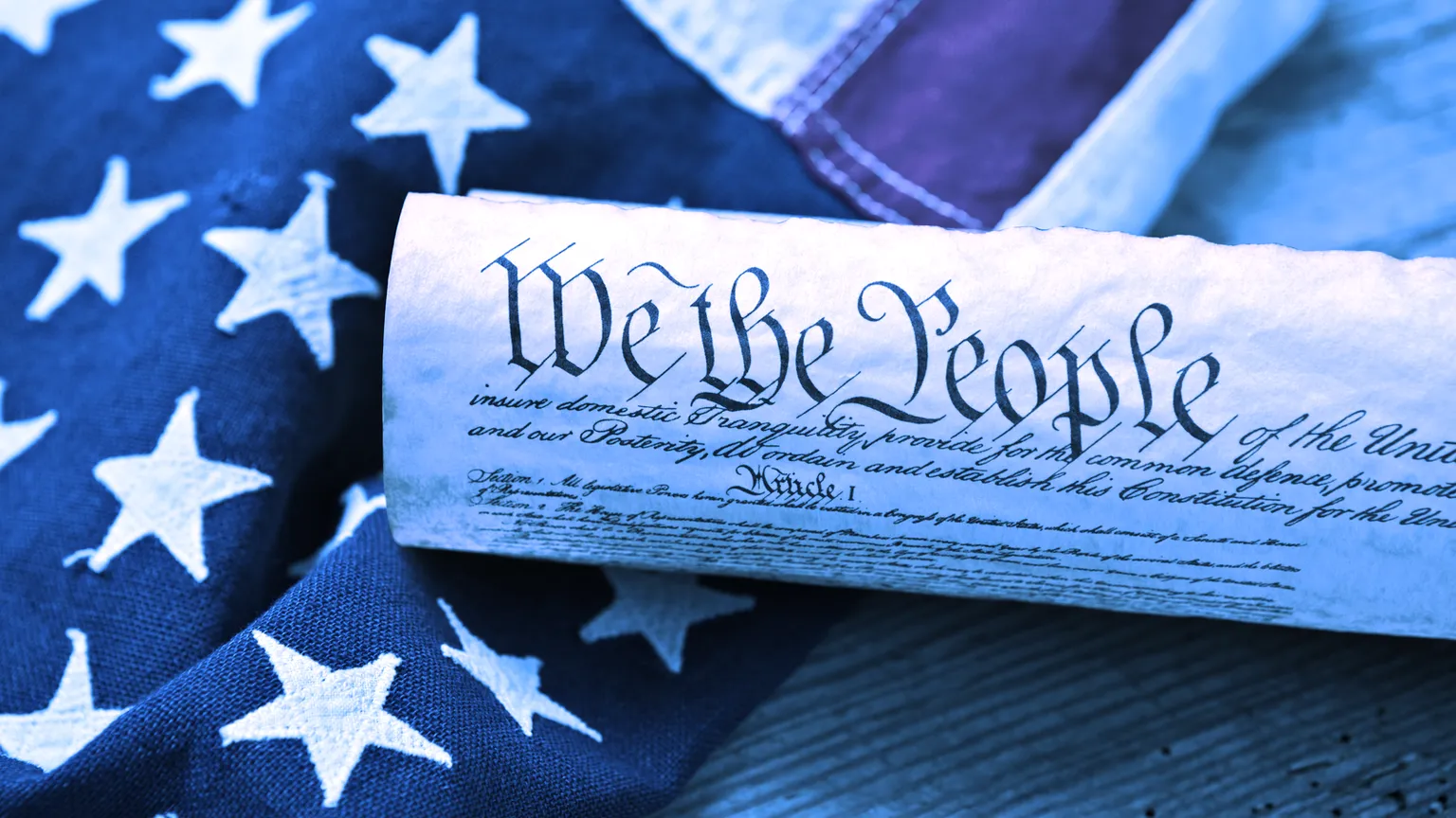 La Constitución de los Estados Unidos, enrollada en un pergamino sobre una bandera americana de época y una tabla de madera rústica. Imagen: Shutterstock