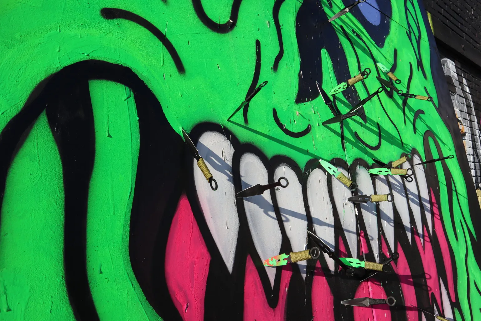 Closeup photograph of Will Carsola's painting of a green demon's mouth, with knives thrown into it.
