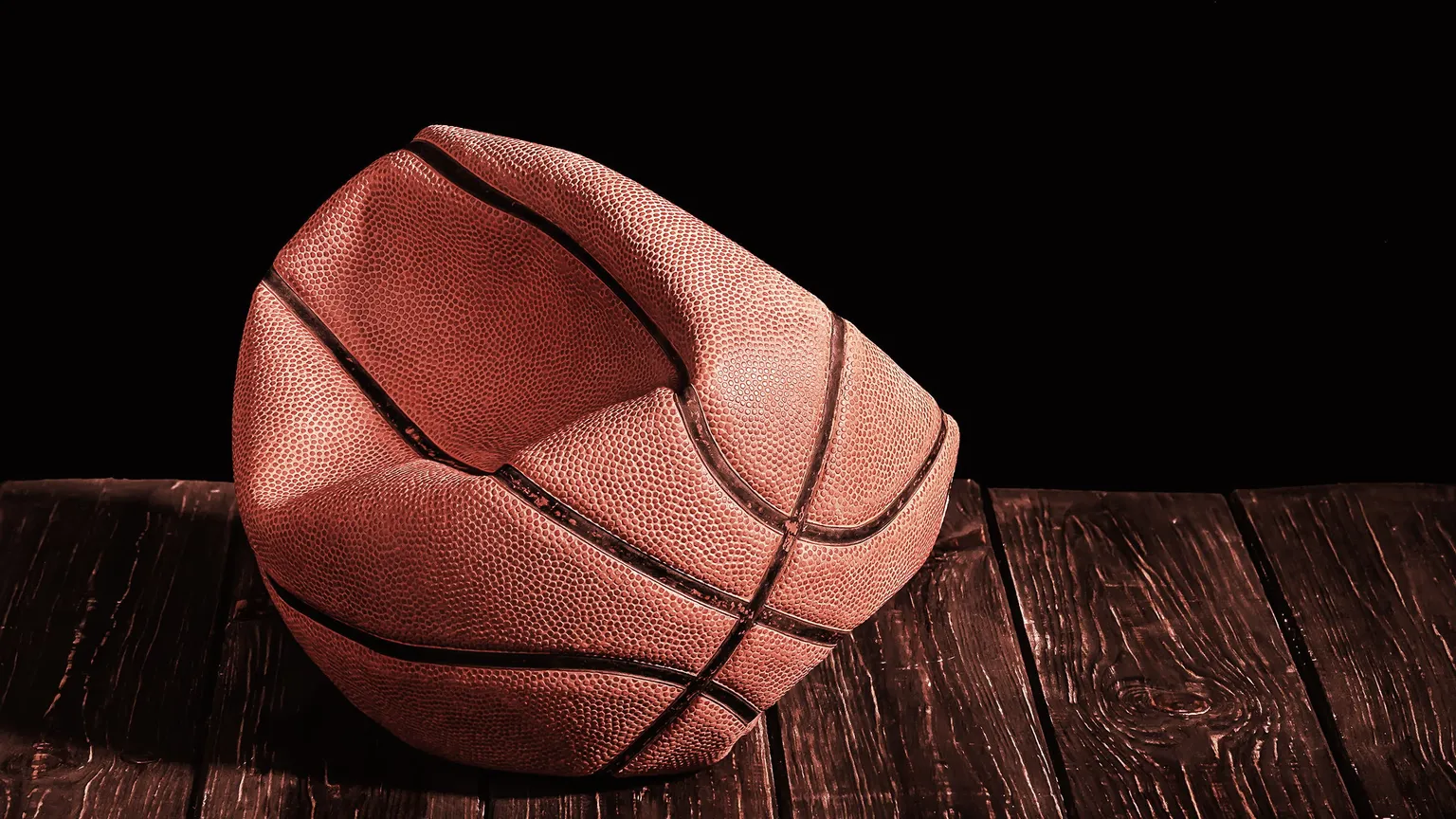 Deflated and rumpled old ball on a wooden floor. Black background.