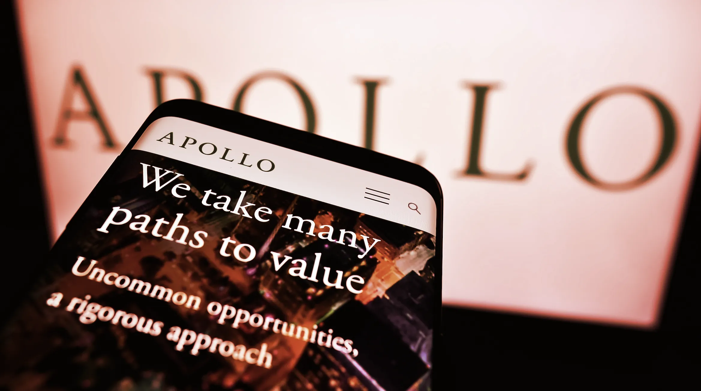 Mobile phone with website of US investment company Apollo Global Management Inc. on screen in front of logo. (Shutterstock)