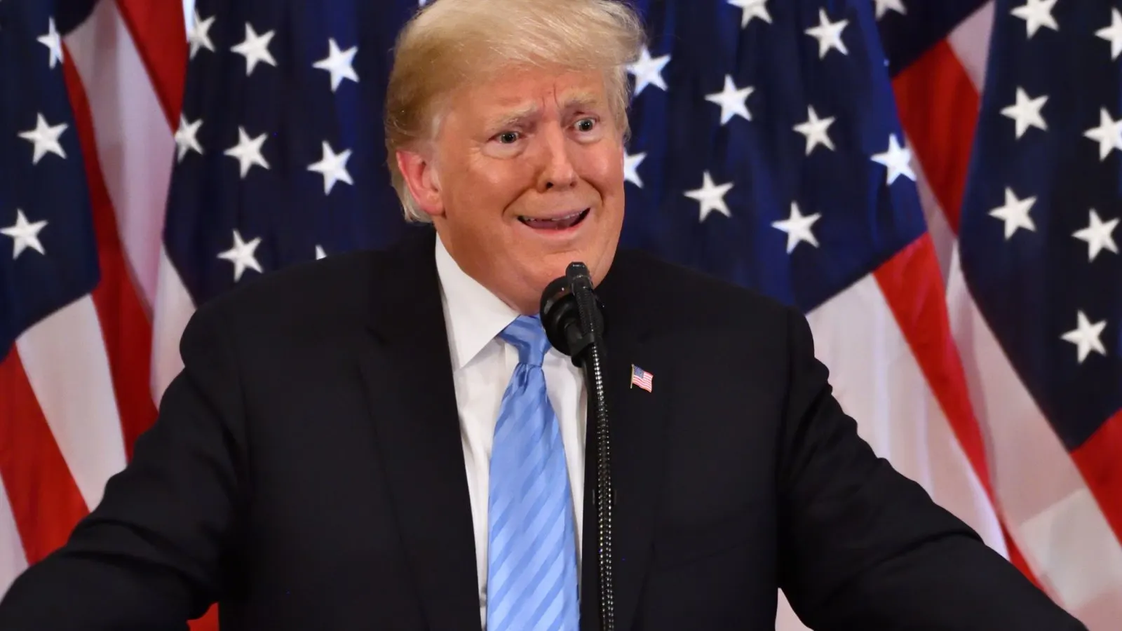 former president donald trump shrugging in front of an american flag