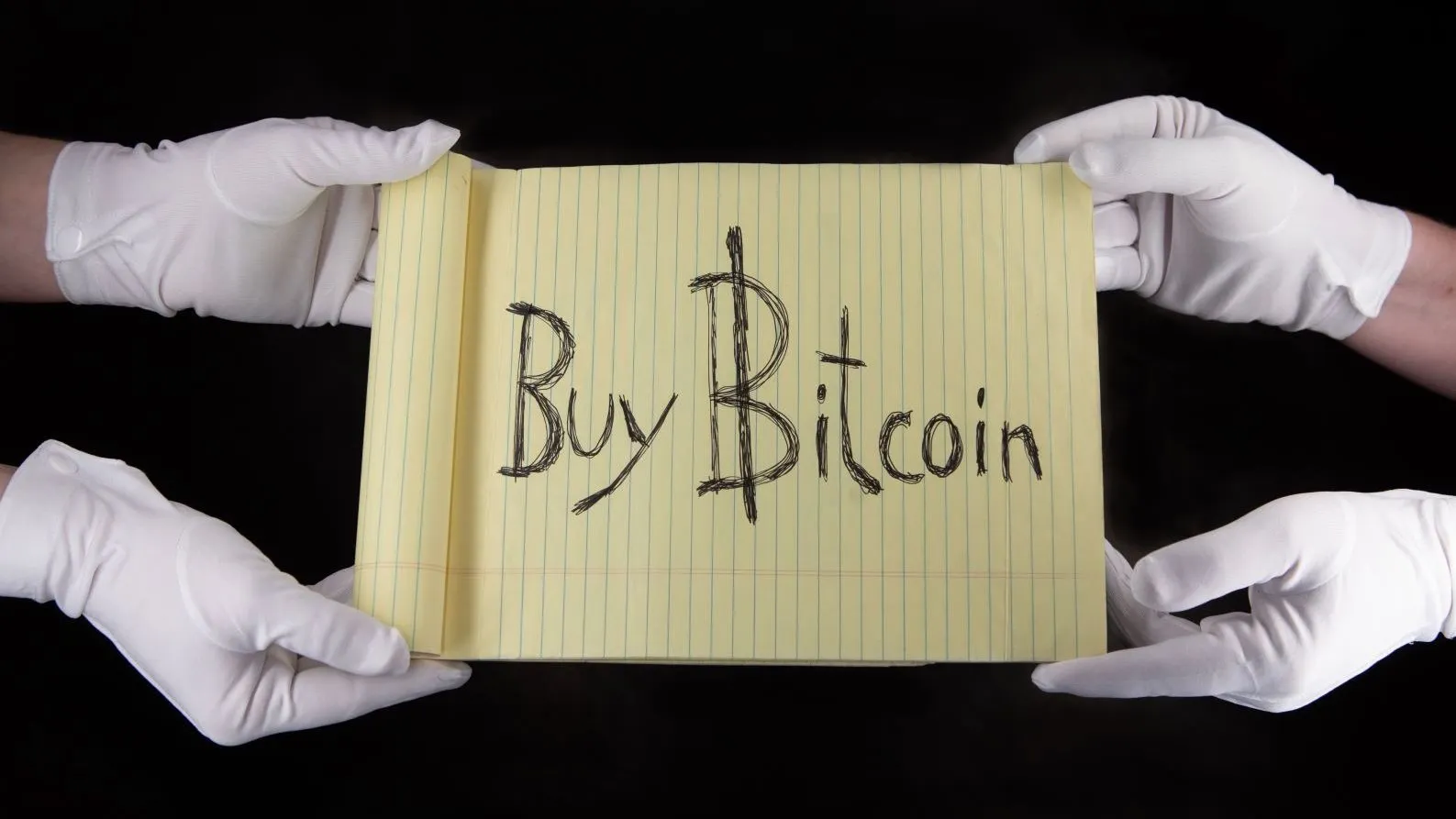 White-gloved hands holding a yellow legal pad with "Buy Bitcoin" written across it.