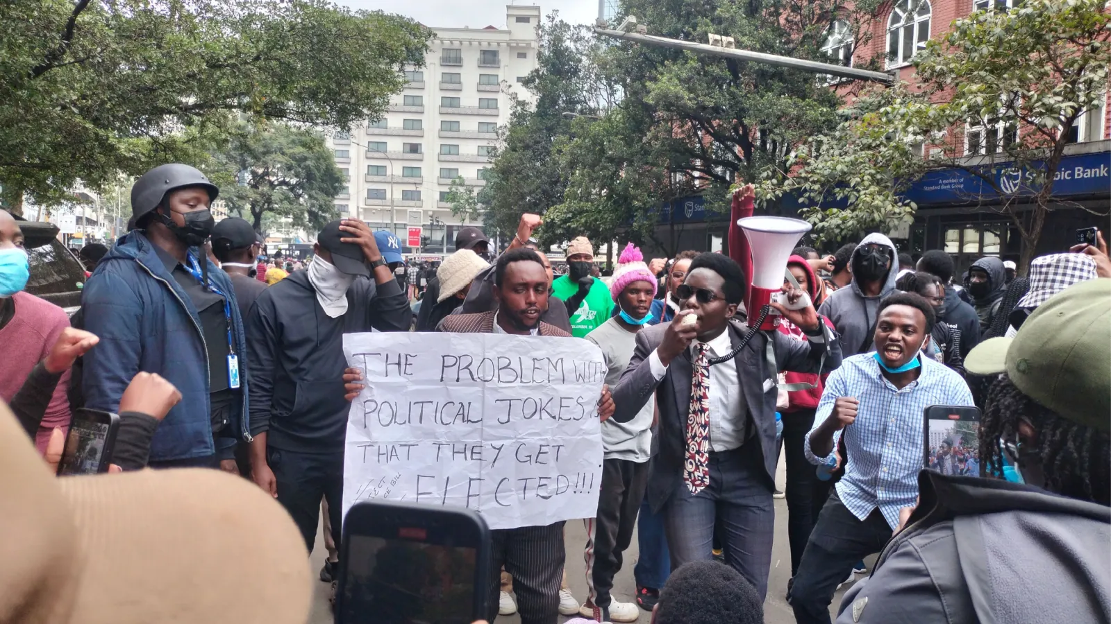 Kenyans protesting the finance bill. One person holds a sign saying 'the problem with political jokes is that they get elected.'
