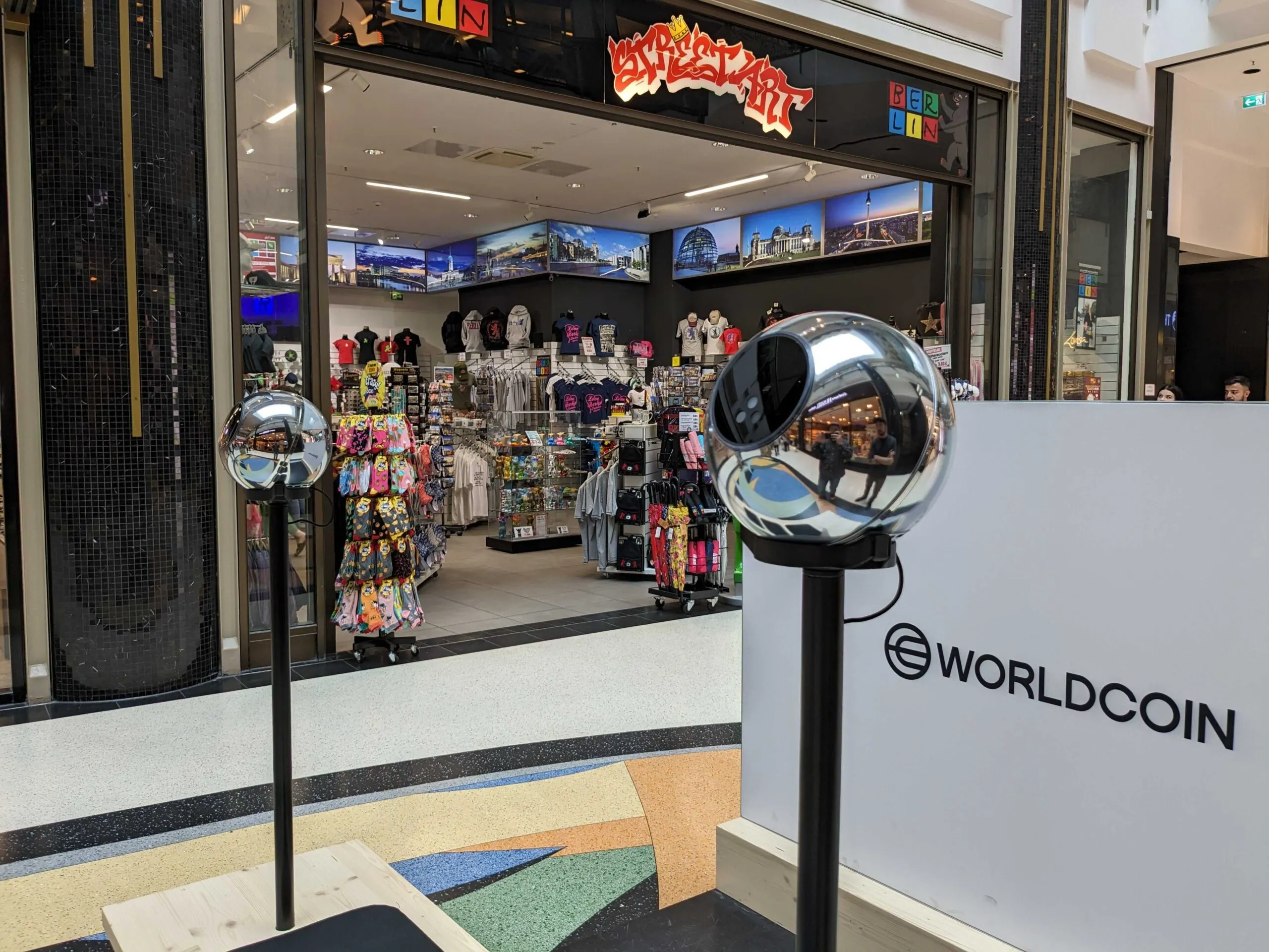 Dos orbes de Worldcoin de pie sobre dos postes en un centro comercial.